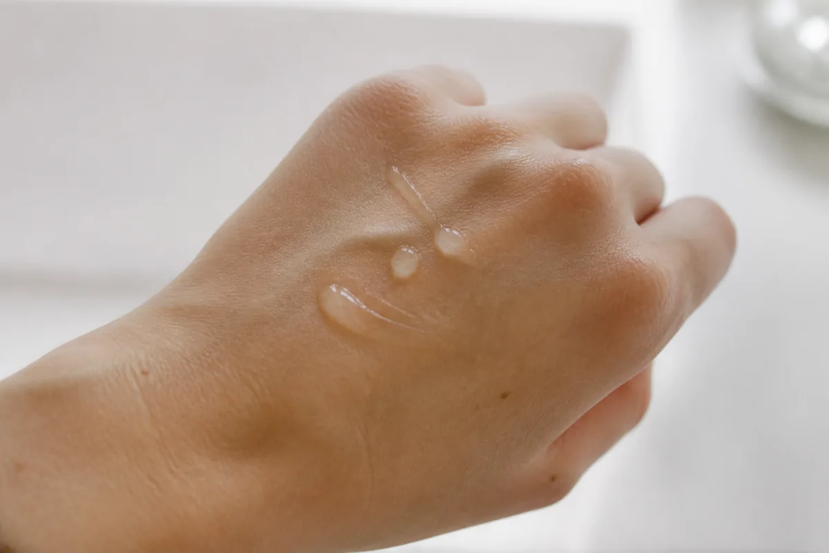 Gouttes de sérum transparent sur le dos de la main d’une femme, représentant l’application d’un soin anti-taches