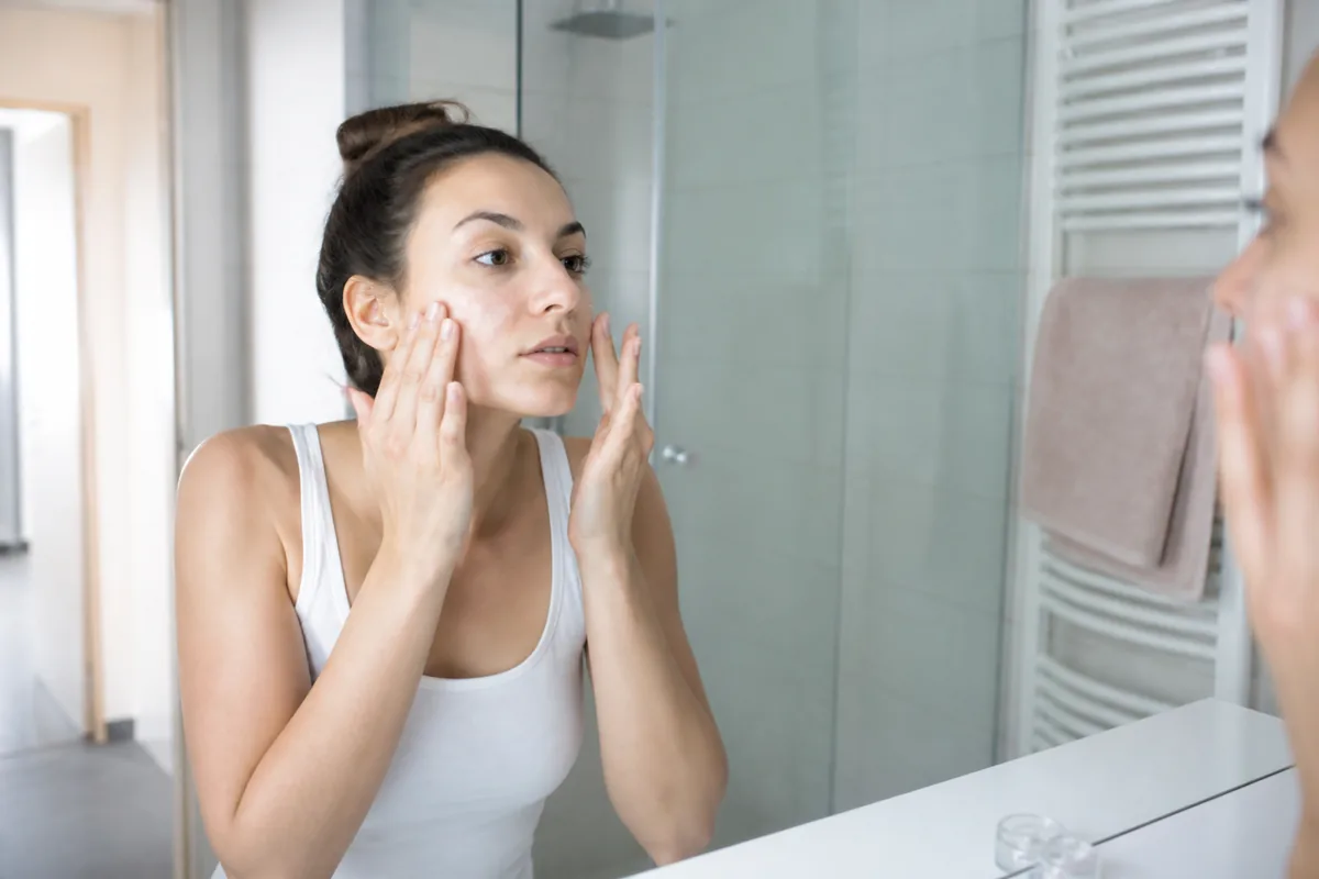 Personne appliquant un gel-crème hydratant sur le visage dans une salle de bain lumineuse